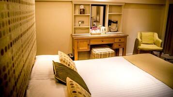 Une chambre d’hôtel comprenant un lit, une commode en bois avec un miroir, une chaise et une petite table avec une bouilloire et des tasses.