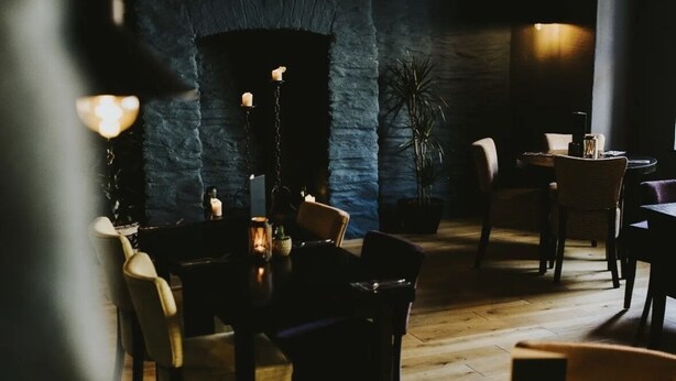 A dimly lit restaurant with stone walls, wooden flooring, and a mix of upholstered and metal chairs.