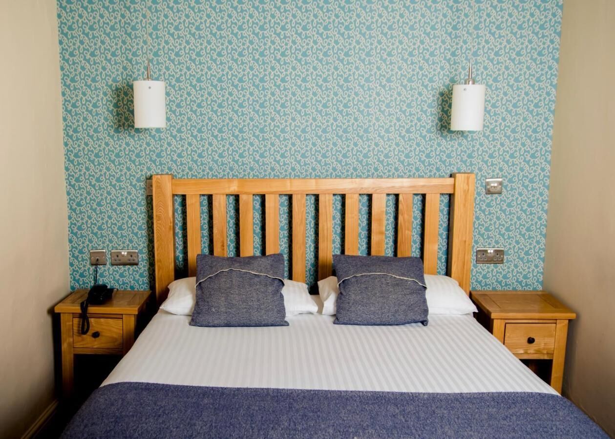 A neatly made bed with a wooden headboard, two bedside tables with lamps, and patterned wallpaper.