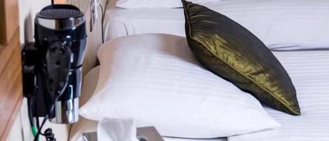 Habitación de hotel con cabecera de madera, ropa de cama blanca y mesita de noche con un dispensador de pañuelos y un dispositivo negro.