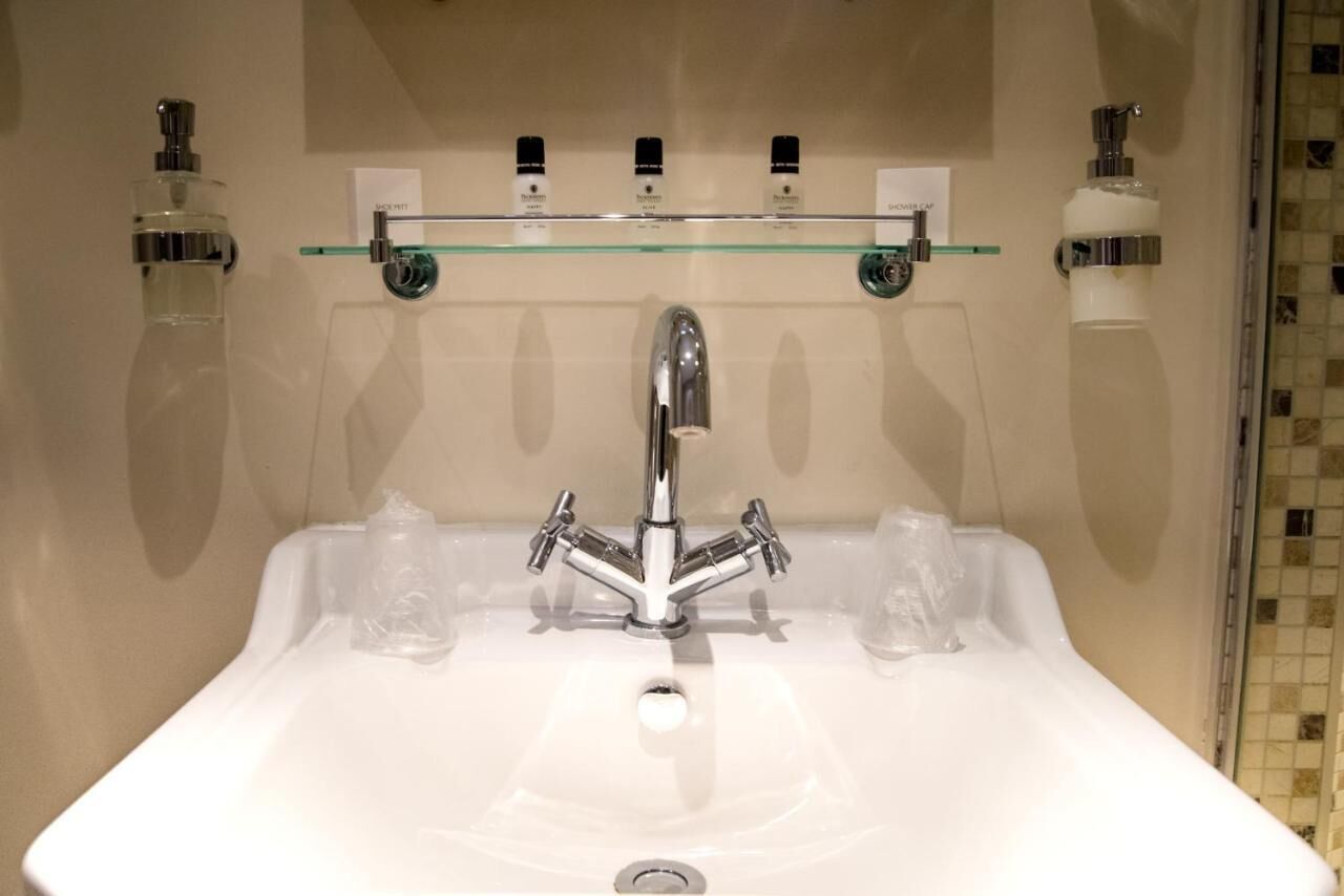 A bathroom with a white sink, chrome faucet, and three glass soap dispensers on a shelf above.
