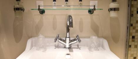 Ein Badezimmer mit einem weißen Waschbecken, einem Chromarmaturen-Set und drei Glas-Seifenspendern auf einem Regal.
