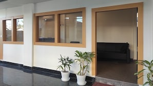 Un pasillo con mostrador de recepción, plantas en macetas y un sofá negro.
