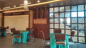 Un salón de conferencias con mesas y sillas, paneles de madera y grandes ventanales con vistas a un edificio y una escalera.