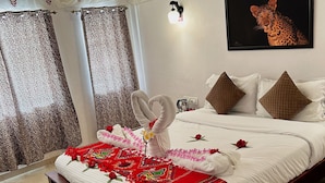 Una cama bien hecha con una colcha de diseño rojo y blanco, un arreglo de toallas en forma de corazón y una obra de arte de estilo leopardo en la pared.