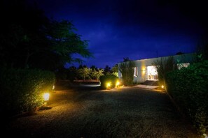 Vue nocturne d’un bâtiment avec une allée en gravier et une entrée illuminée.