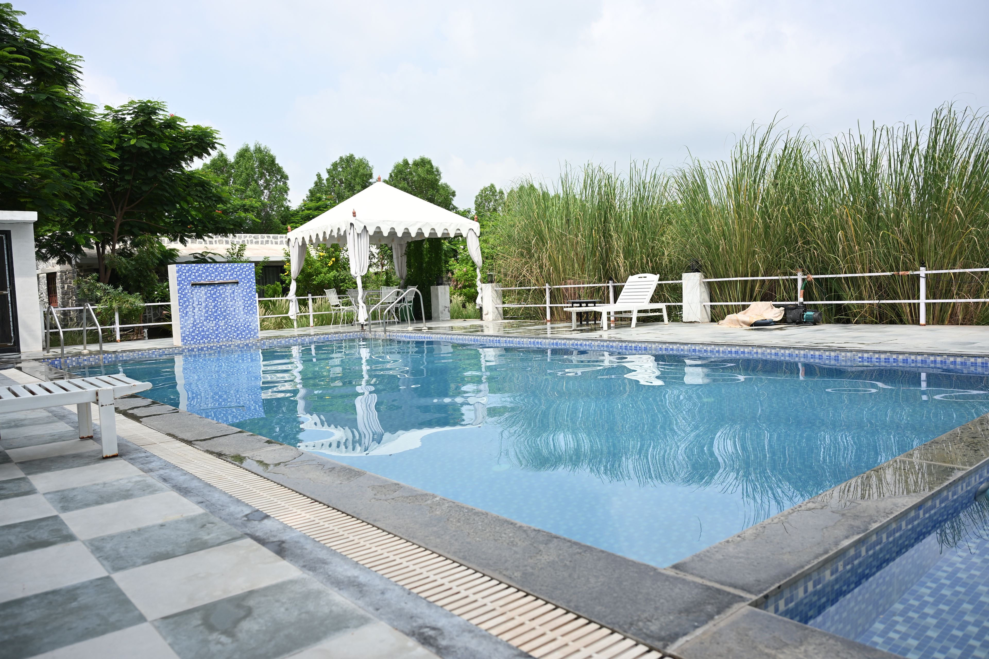 Una piscina con borde de azulejos, sillas de descanso, zona de estar cubierta y una valla.