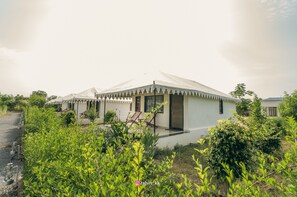 Un bâtiment blanc doté d’un toit plat et d’un petit porche, entouré de verdure.