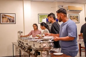 Un buffet avec plusieurs points de service, une personne qui distribue la nourriture et un appareil de climatisation fixé au mur.