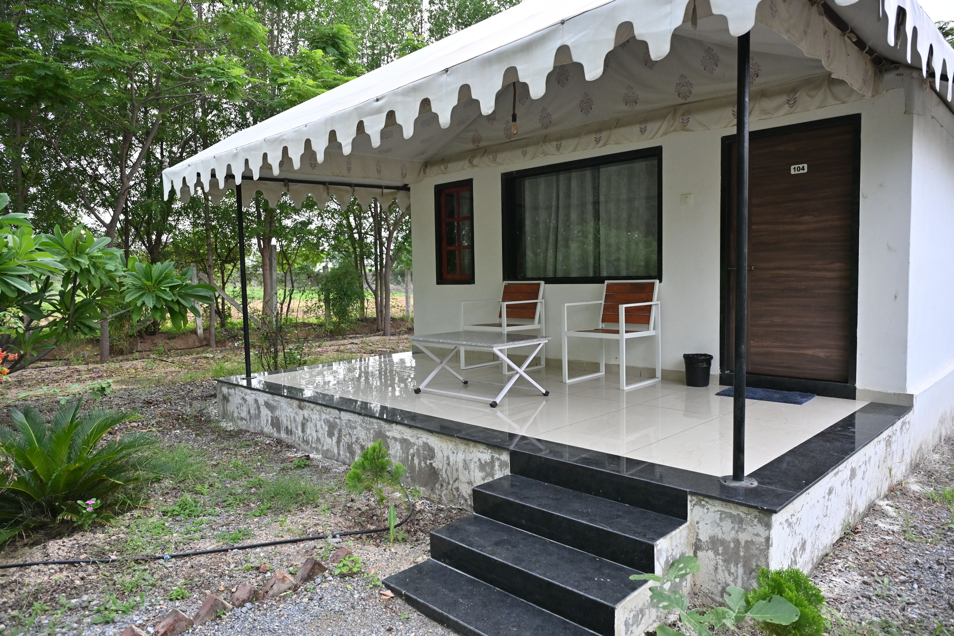 A small, single-story building with a covered porch, two chairs, a table, and a door.