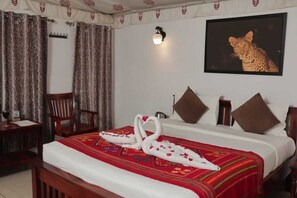 Une chambre d’hôtel avec un lit, un bureau, une chaise, une lampe fixée au mur et un tableau représentant un léopard.