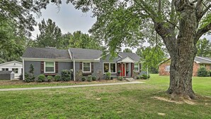 A residential house with a front porch, a large tree in front, and a well-maintained lawn.