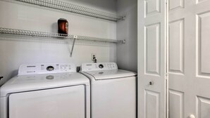 A laundry room with two white front-loading washers and dryers, a metal shelf above, and a white door. - Modern Nashville Townhome: Large Yard & Deck! (Antioch)