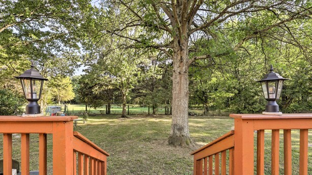 A wooden deck with two lanterns, surrounded by a grassy area and trees. - Modern Nashville Townhome: Large Yard & Deck! (Antioch)