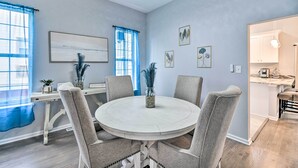 A dining area with a round table, four chairs, and a kitchen visible in the background.