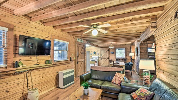 A cozy log cabin interior with a leather sofa, wooden walls, a ceiling fan, and a television mounted on the wall. - Blairsville Cabin w/ Fire Pit, 7 Mi to Dtwn! (Blairsville)