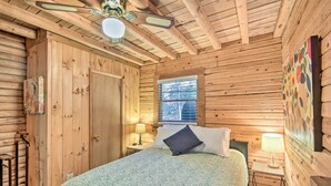 A wooden cabin bedroom with a bed, a window, a ceiling fan, and a wall-mounted lamp. - Blairsville Cabin w/ Fire Pit, 7 Mi to Dtwn! (Blairsville)
