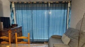 A living room with a wooden dining table, chairs, a sofa, and a TV. - Grand Studio à Quelques pas de la Plage et des Activities de Loisirs (GUIDEL)