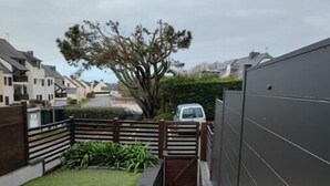 A residential backyard with a paved patio, a wooden fence, and a grassy area. - Grand Studio à Quelques pas de la Plage et des Activities de Loisirs (GUIDEL)