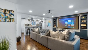 Una sala de estar moderna con un televisor de pantalla plana grande, un sofá gris y una cocina al fondo.