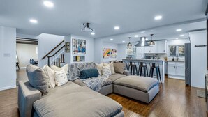 Una sala de estar moderna con un sofá modular, una cocina con armarios blancos y una escalera que sube a otro nivel.