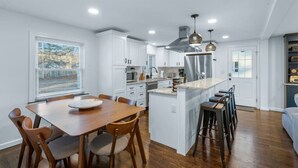 Una cocina moderna con armarios blancos, una isla central con taburetes y una zona de comedor con una mesa y sillas de madera.