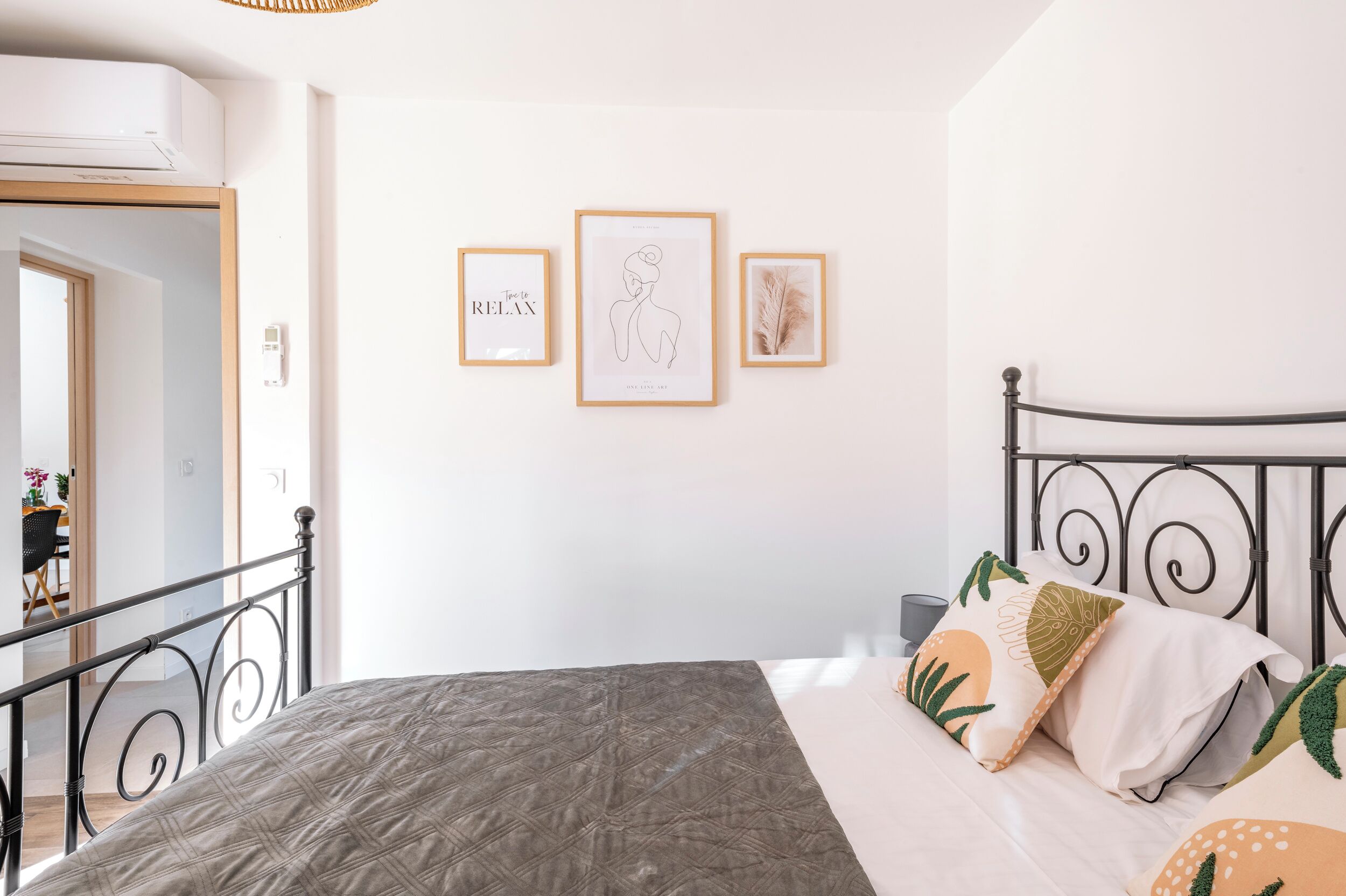 Ein Schlafzimmer mit einem Bett, einem Nachttisch und einer Wand-Klimaanlage. An der Wand hängen drei gerahmte Bilder.