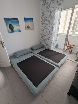 Une pièce comprenant un lit, une petite chaise en bois et une fenêtre ornée de rideaux à motifs floraux.