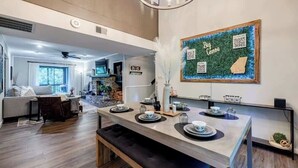A modern kitchen with a dining area, featuring a central island with tea set, a wall-mounted QR code, and a 'Big Canoe' sign. - Pet Friendly Condo with Screened Deck & Fireplace (Jasper)