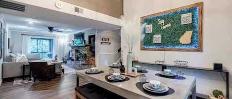 A modern kitchen with a dining area, featuring a central island with tea set, a wall-mounted QR code, and a 'Big Canoe' sign.