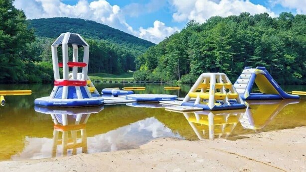 Inflatable water play structures by a lake with a forested hill in the background. - Pet Friendly Condo with Screened Deck & Fireplace (Jasper)