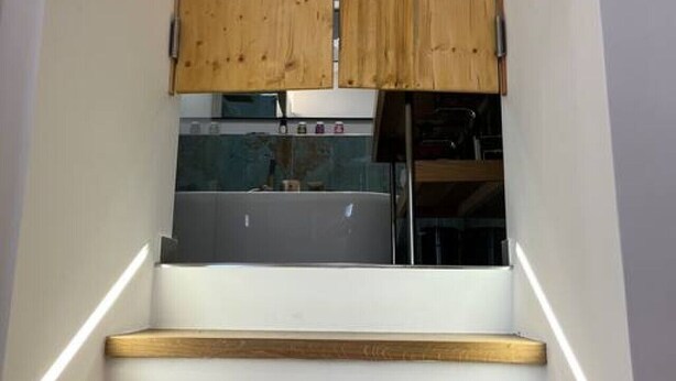 A staircase with wooden steps leading up to a kitchen area with a wooden cabinet and a stainless steel refrigerator. - Newly Renovated Boutique Apartment (Wien)