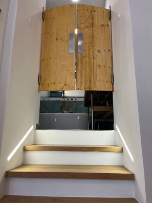 A staircase with wooden steps leading up to a kitchen area with a wooden cabinet and a stainless steel refrigerator. - Newly Renovated Boutique Apartment (Wien)
