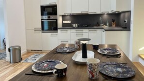 A modern kitchen with white cabinets, a black countertop, and a dining table set with plates, cups, and a candle. - Newly Renovated Boutique Apartment (Wien)