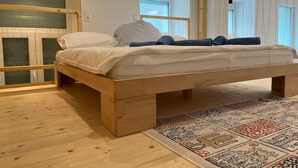 A modern bedroom with a wooden bed, a patterned rug, and a large window with blinds. - Newly Renovated Boutique Apartment (Wien)