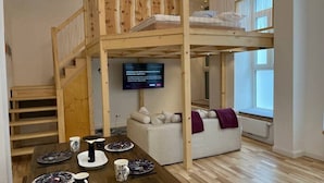 A modern interior with a wooden staircase, a dining area with plates and cups, a sofa with cushions, and a television on the wall. - Newly Renovated Boutique Apartment (Wien)