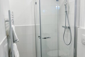 Une douche fermée par des parois en verre, dotée d’un pommeau de douche à main et d’un panneau de commande fixé au mur.