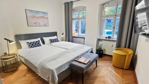 A bedroom with a bed, bedside tables, a bench, a window with curtains, a radiator, and a yellow chair. - Beckhomes: Luxuriöses Juwel Mitten in der Altstadt (Bamberg)