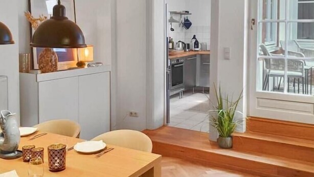 A dining area with a wooden table, chairs, and a pendant light. There is a kitchen visible through an open door in the background. - Beckhomes: Luxuriöses Juwel Mitten in der Altstadt (Bamberg)