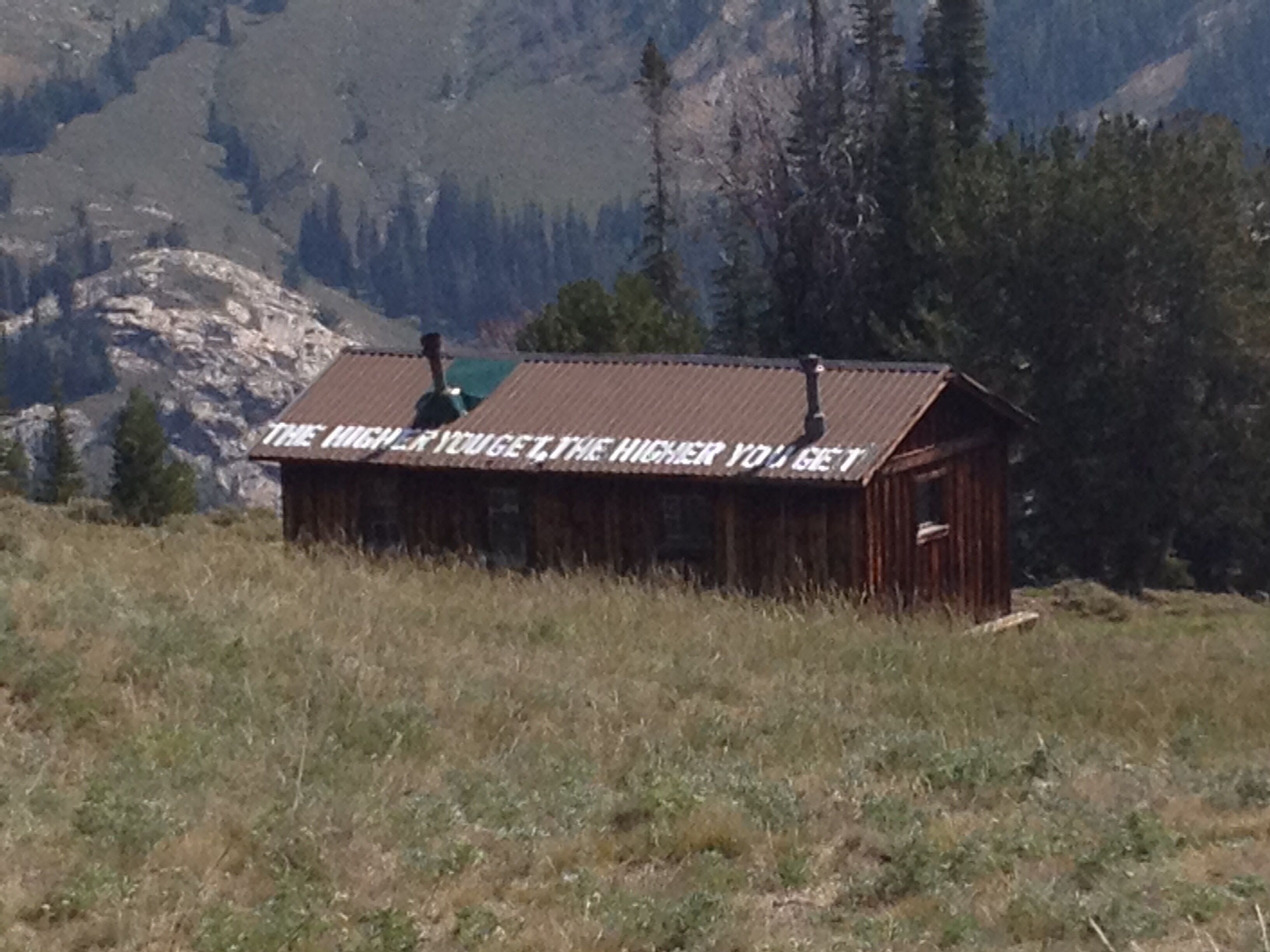 A rustic cabin with a sign that reads "THE HIGHER YOU GET, THE HIGHER YOU GET."