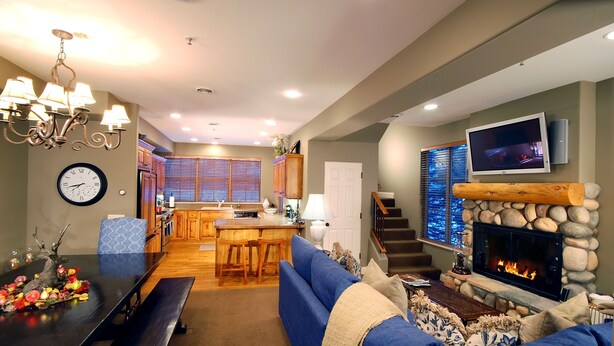 A modern living room with a fireplace, blue sofa, dining table, and kitchen in the background.