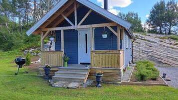 A small, single-story cabin with a wooden deck, a front porch, and a chimney.