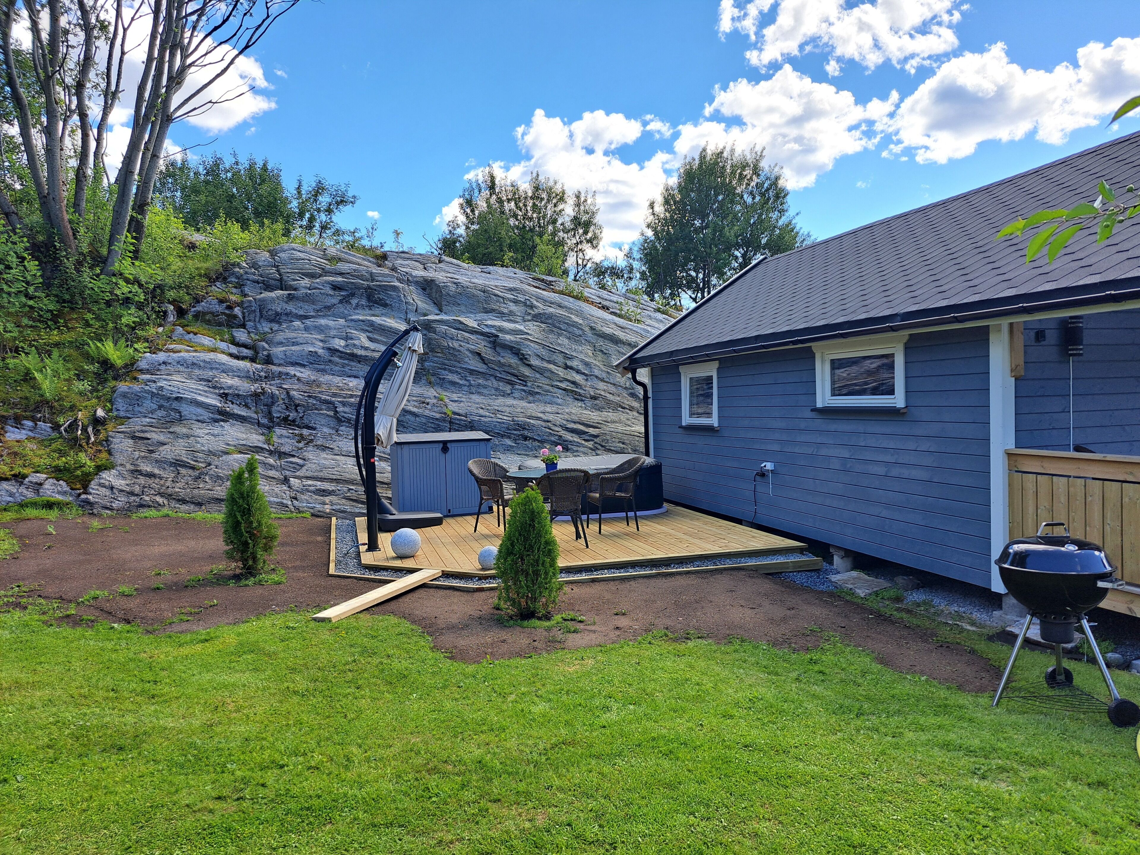 A house with a deck, a barbecue grill, and a rock formation in the background.