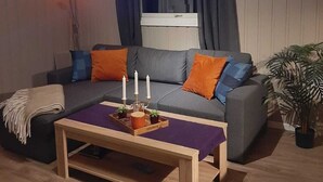 Un salon chaleureux avec un canapé gris, des coussins orange et bleus, une table basse en bois ornée de bougies et une plante en pot.