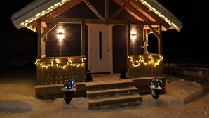 Une cabane en bois avec un toit en pente, illuminée par des guirlandes lumineuses, et entourée de neige.