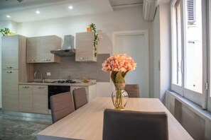 Una cocina moderna con una mesa y sillas, un florero con flores, y una ventana con persianas.