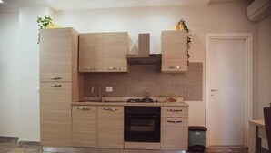 Eine kleine Küche mit hellen Holzschränken, einem Einbauofen und einer Spüle aus Edelstahl.
