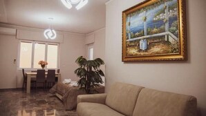 Ein Wohnzimmer mit beiger Couch, einem Essbereich mit Tisch und Stühlen, einer großen Topfpflanze und einem Gemälde an der Wand.