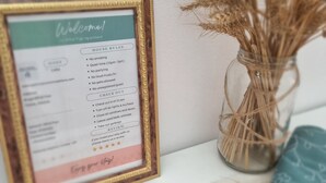 A framed house rules sign with check-out instructions and a review request, placed on a table next to a vase with dried plants. - Mihal Popi Apartment (Tirana)