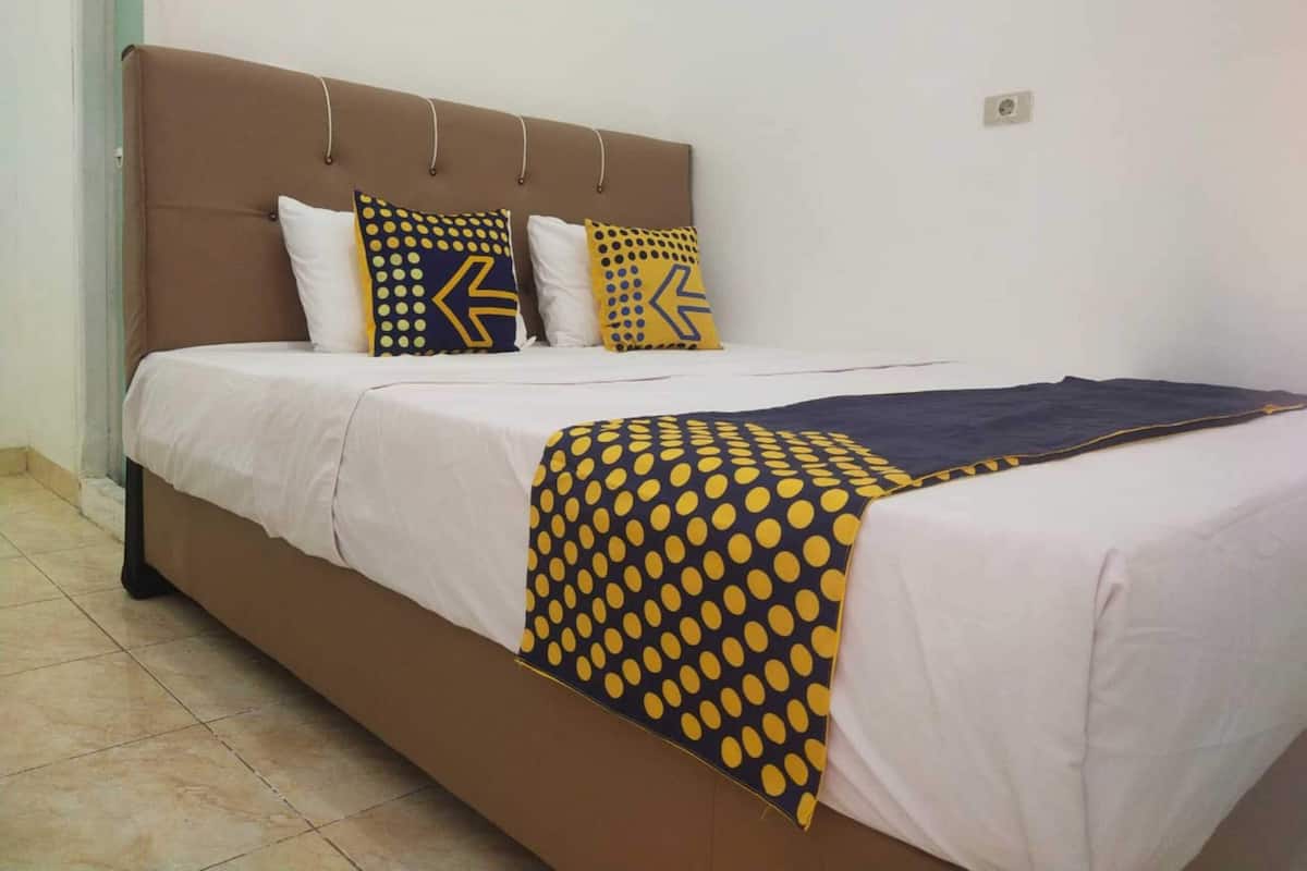 A bed with a brown headboard, white bedding, and patterned pillows.